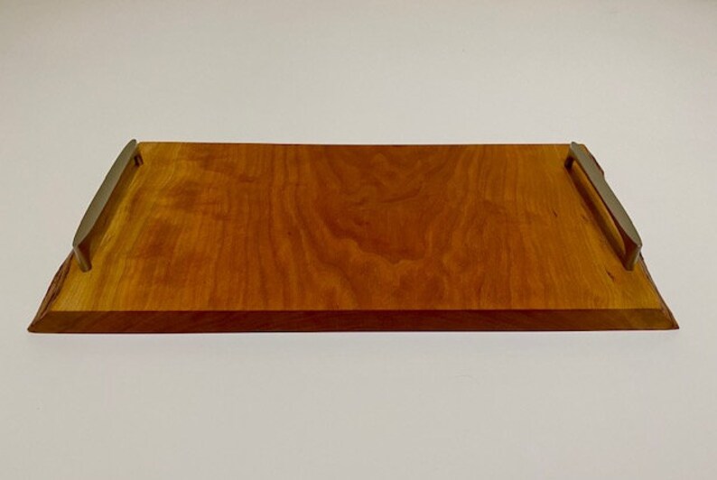 Op de afbeelding: Een rechthoekige houten dienblad met een natuurlijke houten afwerking en twee metalen handvatten. Het dienblad heeft een glad oppervlak en is perfect om eten of drinken te serveren.