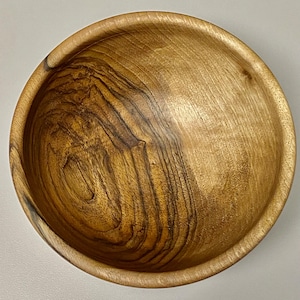 May include: A large, wooden bowl with a natural, light brown finish. The bowl has a deep, rounded shape and a smooth, polished surface. The wood grain is visible and adds a rustic touch to the bowl.
