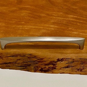 Op de afbeelding: Een houten serveerschaal met een natuurlijke rand en een zilveren metalen handvat.
