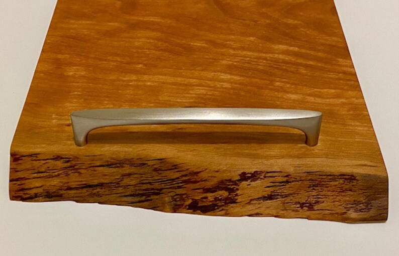Op de afbeelding: Een houten serveerschaal met een natuurlijke rand en een zilveren metalen handvat.