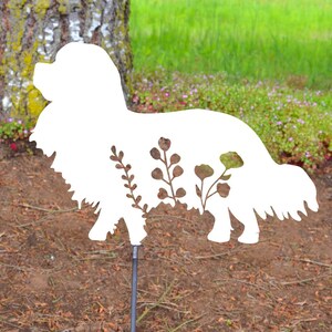 Può includere: Silhouette di cane in metallo bianco con disegni floreali ritagliati. La silhouette è montata su un paletto in metallo nero.