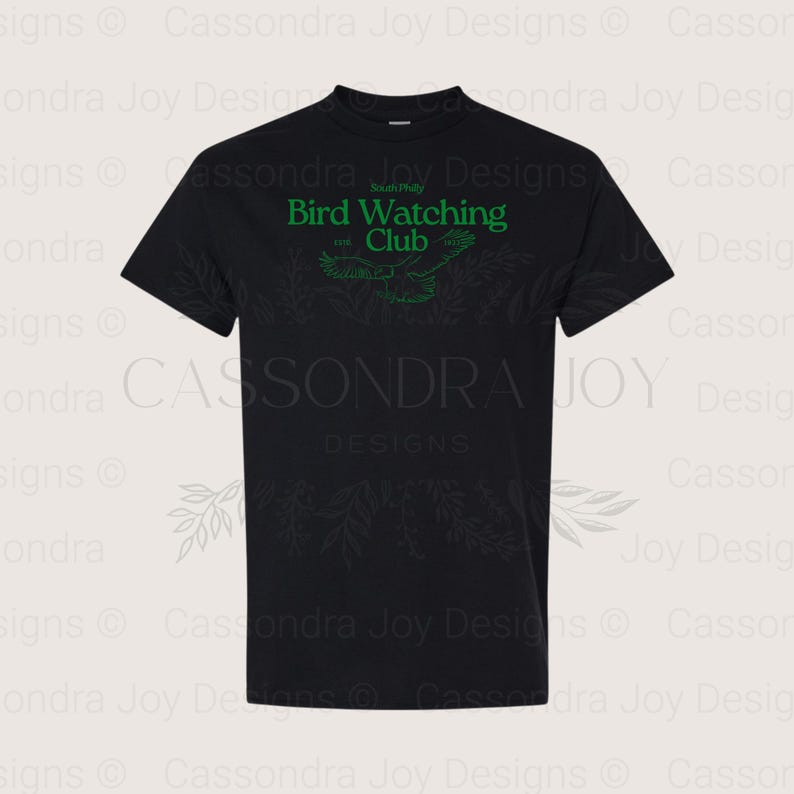 Puede incluir: Una camiseta negra de manga corta con texto verde que dice South Philly Bird Watching Club, con los a&ntilde;os 1998 y 2023 a ambos lados de un dibujo lineal de un p&aacute;jaro en vuelo, centrado en la zona del pecho de la prenda.