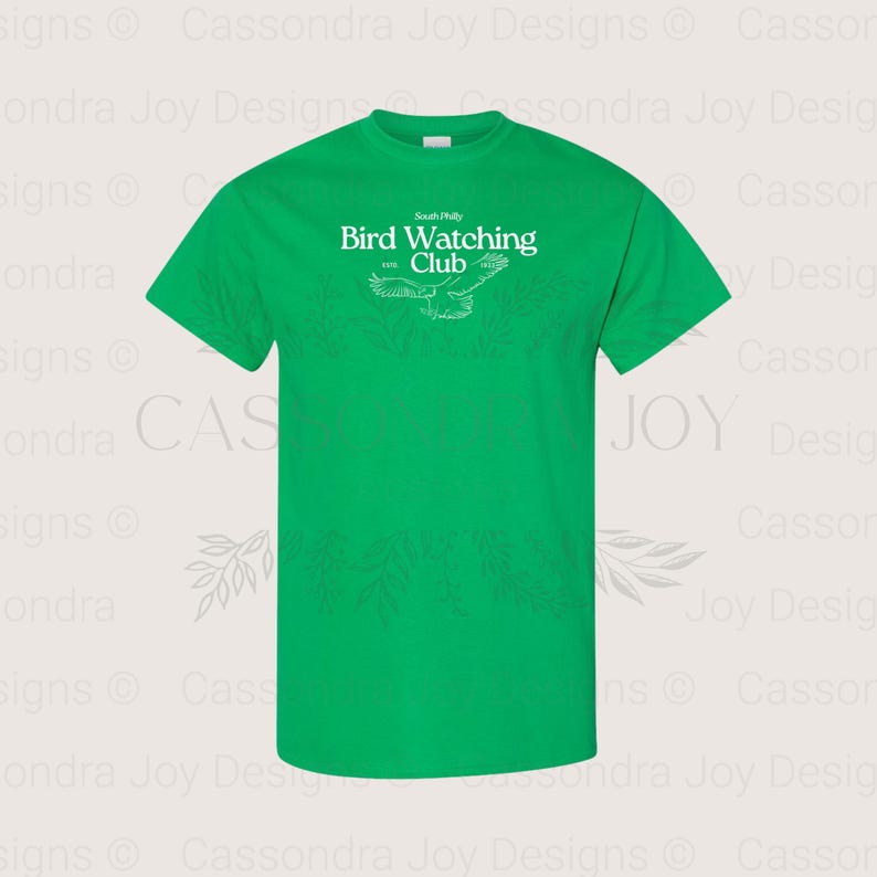 Puede incluir: Una camiseta de manga corta de color verde brillante con texto blanco que dice South Philly Bird Watching Club ESTD 1992. Debajo del texto hay un dibujo lineal blanco de un p&aacute;jaro en vuelo con las alas extendidas en el centro del pecho.