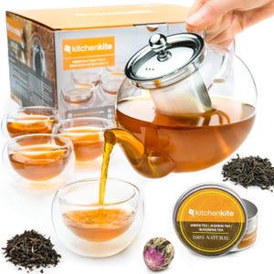 May include: A clear glass teapot with a stainless steel infuser and lid, pouring tea into a double-walled glass cup. The set includes several cups, a box, and a tin of tea. The tea is amber-colored, and loose tea leaves are visible.