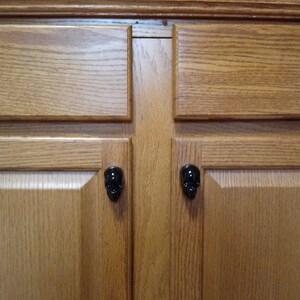 May include: Close-up of a wooden cabinet with four black skull-shaped cabinet knobs.