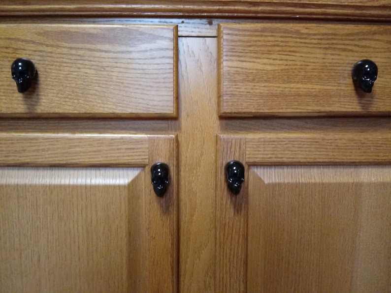 May include: Close-up of a wooden cabinet with four black skull-shaped cabinet knobs.