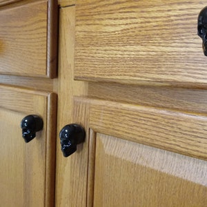 May include: Close-up of wooden cabinet doors with black skull-shaped drawer pulls.