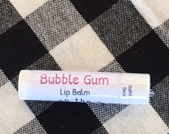 May include: A white lip balm tube with the words "Bubble Gum Lip Balm" in pink lettering. The tube is lying on a black and white checkered surface. The words "Safety Seal" are printed on the side.