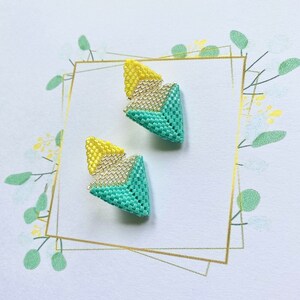 May include: A pair of geometric earrings with a yellow, white, and turquoise color scheme. The earrings are made of small beads and have a triangular shape.