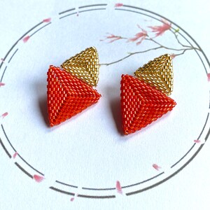 May include: A pair of geometric earrings with a red and gold design. The earrings are made of small beads and are shaped like triangles.