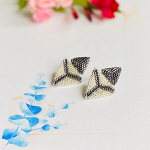 May include: A pair of silver and black geometric triangle earrings. The earrings are made of small beads and are designed in a layered, three-dimensional style.