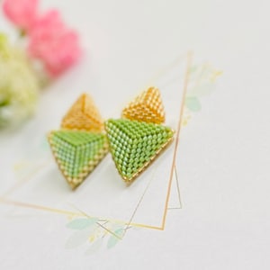 May include: A pair of green and gold triangle-shaped earrings made of beads. The earrings are small and delicate.
