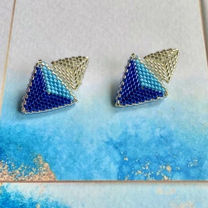 May include: A pair of blue and silver triangle shaped earrings. The earrings are made of small beads and have a geometric design.