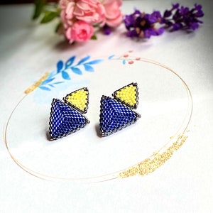 May include: A pair of blue and yellow triangle shaped earrings. The earrings are made of small beads and are a geometric design.