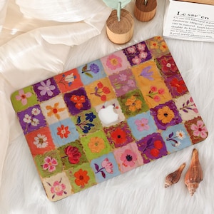 May include: A colorful laptop case featuring a patchwork design of various flowers in squares. The case has a white Apple logo and is set against a white, fluffy background. The flowers are in shades of pink, orange, purple, and yellow.