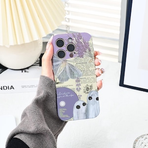 Peut inclure: Une coque de téléphone violette et blanche avec un motif floral, un papillon et des fantômes. La coque a un style vintage et présente un texte qui dit "Bridesmaids never in the shade".
