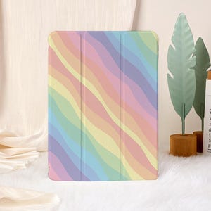 Op de afbeelding: Een tablet hoesje met een pastelkleurig regenboog golfstreepjespatroon. De hoes is een zachte hoes, waarschijnlijk gemaakt van flexibel materiaal, en is ontworpen om een tablet te beschermen. De kleuren zijn onder meer roze, geel, blauw en groen.