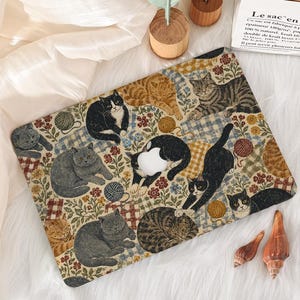 Op de afbeelding: Een rechthoekige laptopskin met een herhalend patroon van diverse katten in zwart, grijs, bruin en cyperse kleuren. De katten worden afgewisseld met kleurrijke bloemmotieven, geblokte vierkanten en bollen wol op een lichte achtergrond.
