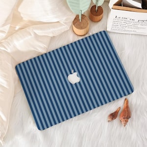 May include: A laptop skin featuring a pattern of alternating dark blue and light blue vertical stripes. The skin is applied to the lid of a laptop, which displays a centered white Apple logo. The design covers the entire surface of the laptop lid.