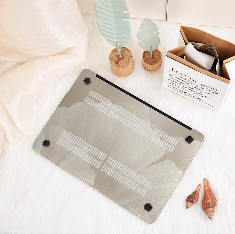 May include: A silver laptop case with a cloud-like design. The case has a black border and four black rubber feet. The bottom of the case has ventilation slots. The case is on a white, fluffy surface.
