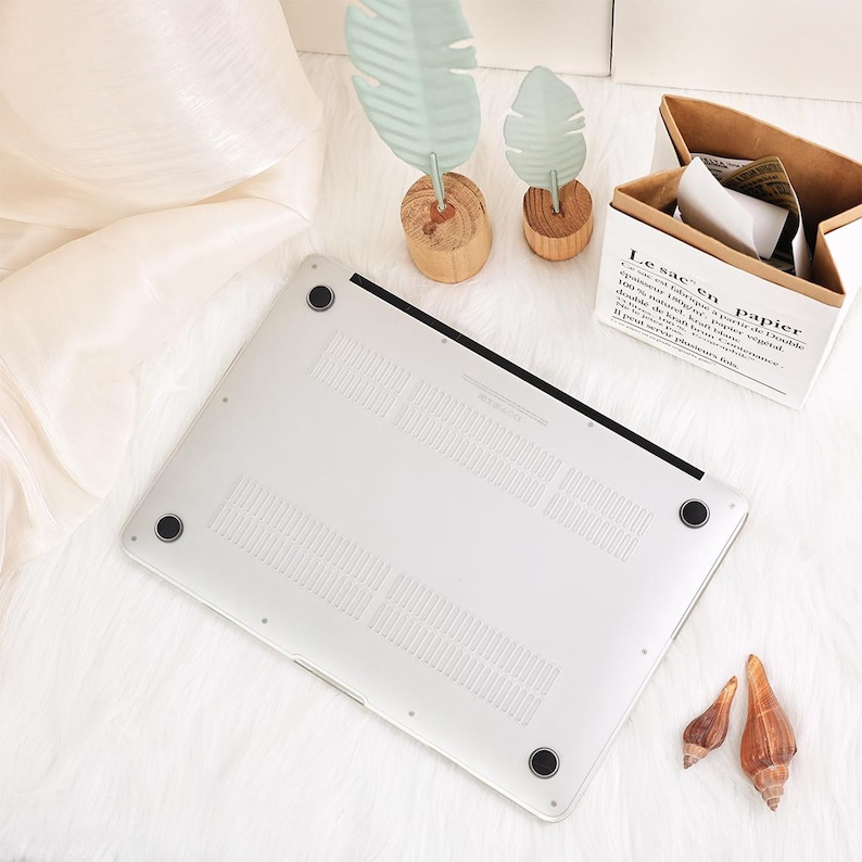 May include: A silver laptop computer with a black border and four black rubber feet. The laptop is on a white, fluffy surface. Decorative leaf ornaments and a paper box are in the background.