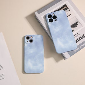 Puede incluir: Dos fundas para teléfono de color azul claro con un diseño de nubes blancas. Las fundas tienen una protuberancia de cámara elevada con tres lentes.