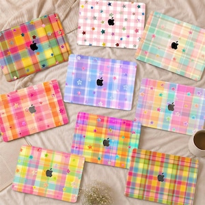 May include: Eight rectangular laptop covers featuring various plaid patterns in vibrant colors, each decorated with scattered small star shapes and a central black Apple logo cutout. The designs include pink, yellow, blue, orange, and green hues.