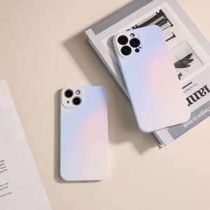 May include: Two white phone cases with a gradient of pink and blue. The cases have a camera lens cutout on the back.