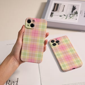 May include: Two phone cases with a plaid pattern in shades of pink, green, and yellow. One case is held in a hand, while the other lies flat. The cases have a smooth finish and are designed for a smartphone.