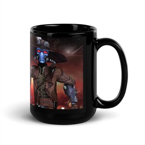 May include: Black ceramic mug featuring a colourful image of a fictional character wearing a cowboy hat and holding a gun. The character has blue skin and red eyes. The background is a red and orange nebula with stars.
