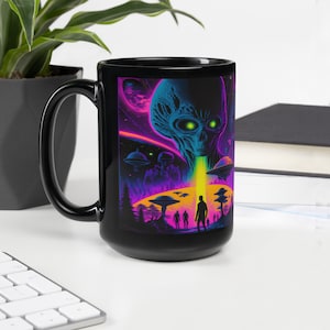 May include: Black ceramic mug with a colorful graphic of an alien with glowing green eyes and a beam of light coming from its mouth. The alien is surrounded by flying saucers and silhouettes of people looking up at the alien.