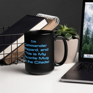 Puede incluir: Taza de cerámica negra con una inscripción blanca que dice "Soy el Comandante Shepard, y esta es mi taza favorita en la Ciudadela".