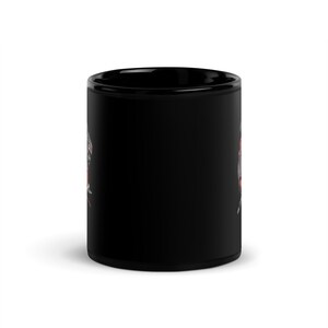 Puede incluir: Una taza de caf&eacute; de cer&aacute;mica negra con un dise&ntilde;o gr&aacute;fico blanco y rojo. El dise&ntilde;o presenta una imagen estilizada de una calavera con una corona y huesos cruzados.