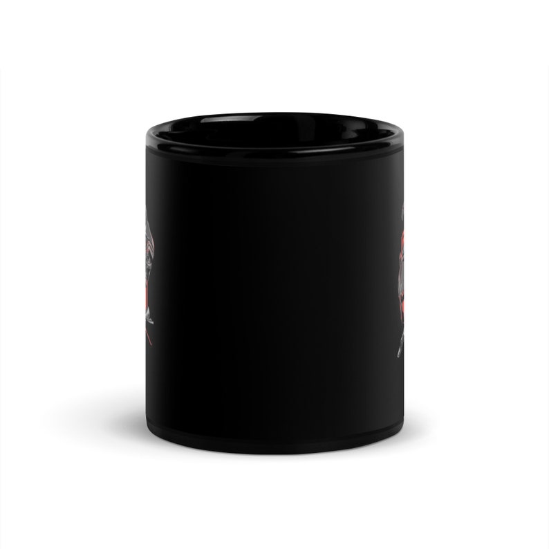 Puede incluir: Una taza de caf&eacute; de cer&aacute;mica negra con un dise&ntilde;o gr&aacute;fico blanco y rojo. El dise&ntilde;o presenta una imagen estilizada de una calavera con una corona y huesos cruzados.