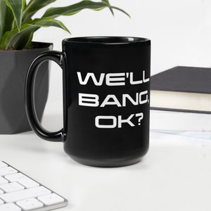 Op de afbeelding: Zwarte keramische mok met een witte inscriptie die "WE'LL BANG, OK?" luidt.