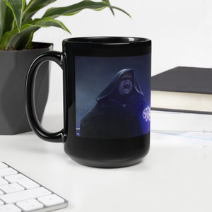 May include: Black ceramic coffee mug with a dark blue and purple image of a hooded figure with glowing hands. The figure has a menacing expression.