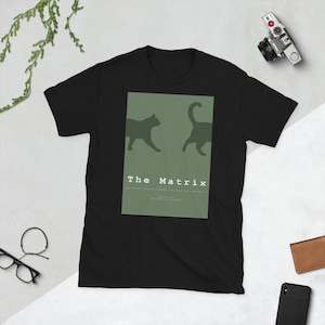 Peut inclure: T-shirt noir avec un rectangle vert orné de deux silhouettes de chats et du texte "The Matrix". Le design comprend les noms des acteurs et du réalisateur. Un tee-shirt décontracté à manches courtes.