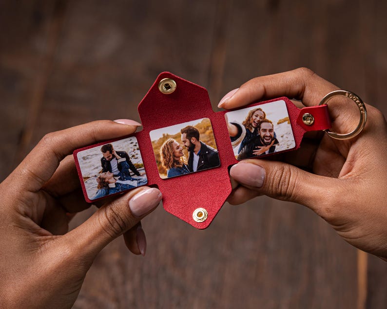 May include: A red leather keychain with a fold-out design. The keychain has three small photo slots, each displaying a different picture of a couple. The keychain has a gold-coloured metal ring.