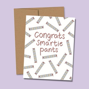 May include: A white card with a pattern of colorful candy rolls. The text "Congrats Smartie pants" is written in brown on the card.