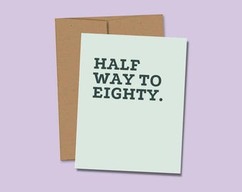 May include: A light green greeting card with the dark text HALF WAY TO EIGHTY. printed in a bold, sans-serif font. The card is positioned in front of a plain, light brown paper envelope, creating a simple and clear visual presentation.