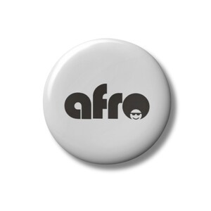 May include: A white button with the word "afro" in dark gray, stylized font. The "o" in "afro" is replaced with a silhouette of a person with an afro and sunglasses. The button is round and has a glossy finish.