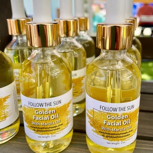 May include: Two amber glass bottles with gold lids and droppers filled with golden facial oil. The bottles have white labels with the text "FOLLOW THE SUN Golden Facial Oil With Marula Oil www.followthesunsoaps.shop IG: @followthesunsoaps Net Weight: 2 oz."