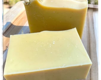 May include: Two bars of handmade soap, one with dried flowers on top. The soap is a pale yellow color and has a smooth, slightly textured surface.