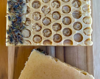 May include: Two bars of handmade soap, one with a honeycomb design and lavender buds, the other plain. Both are a light yellow color.