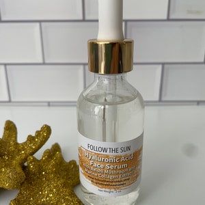 May include: A clear glass bottle with a gold lid and a white dropper top. The bottle is labeled "FOLLOW THE SUN Hyaluronic Acid Face Serum With Reishi Mushroom and Marine Collagen Extract www.followthesunsoaps.shop IG: @followthesunsoaps Net Weight: 2 oz."