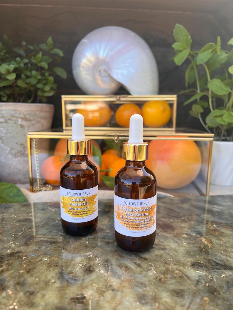 May include: Two amber glass bottles with gold lids and droppers. The bottles are labeled "Follow the Sun" and contain "Golden Facial Oil with Marula Oil" and "Hyaluronic Acid Face Serum with Reishi Mushroom and Marine Collagen Extract".