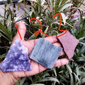 May include: Three flat, irregular stone slabs labelled with the numbers 1, 2, and 3. The first slab is purple with white marbling, the second is a dark grey-blue with a textured surface, and the third is a reddish-brown with a speckled appearance.