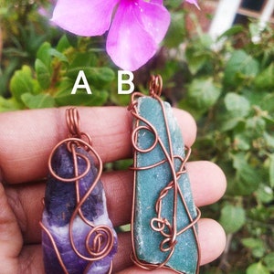 May include: Two wire-wrapped pendants labeled A and B. Pendant A is a rough, deep purple amethyst stone. Pendant B is a flat, rectangular piece of seafoam green stone. Both are encased in copper wire with a loop at the top for hanging.