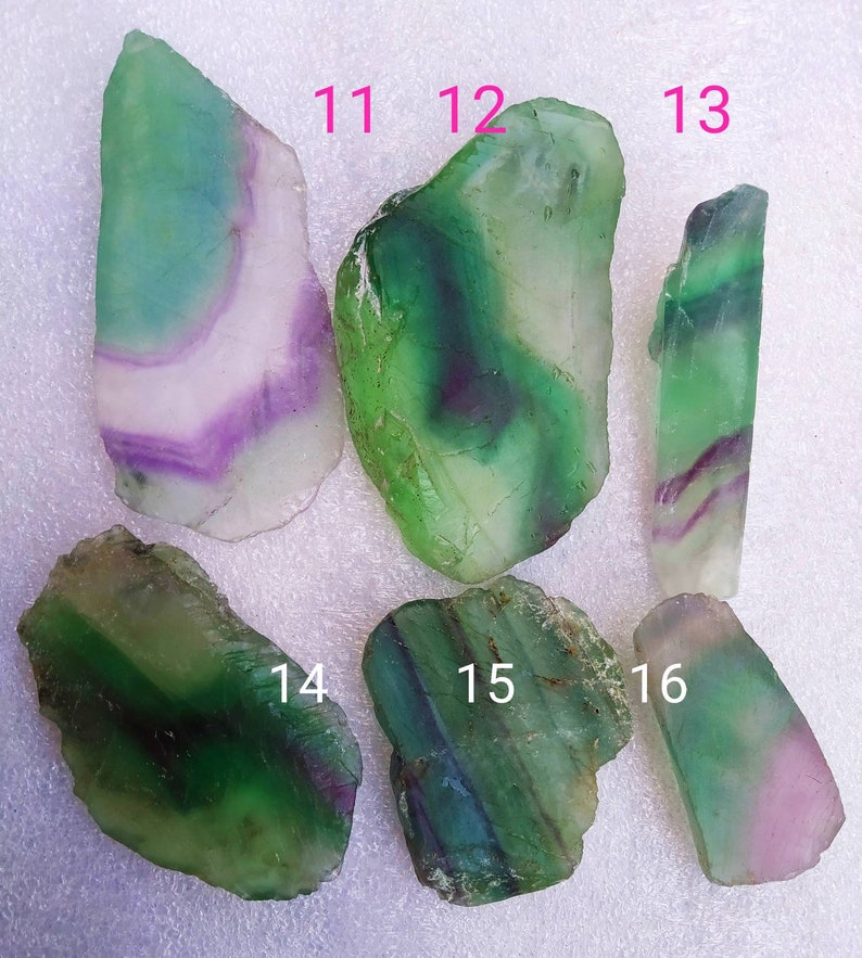 May include: Six polished fluorite slices labeled 11 through 16. Each piece displays translucent bands of green, purple, and white. The stones have irregular, organic shapes with smooth, flat surfaces and varying color intensities throughout each specimen.