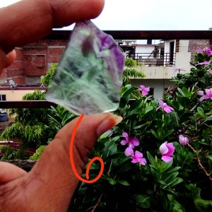 Puede incluir: Un trozo de cristal de fluorita transl&uacute;cido de forma irregular que presenta bandas distintivas de color verde claro y morado intenso. El esp&eacute;cimen mineral muestra una superficie lisa y pulida con fracturas internas visibles y zonificaci&oacute;n.